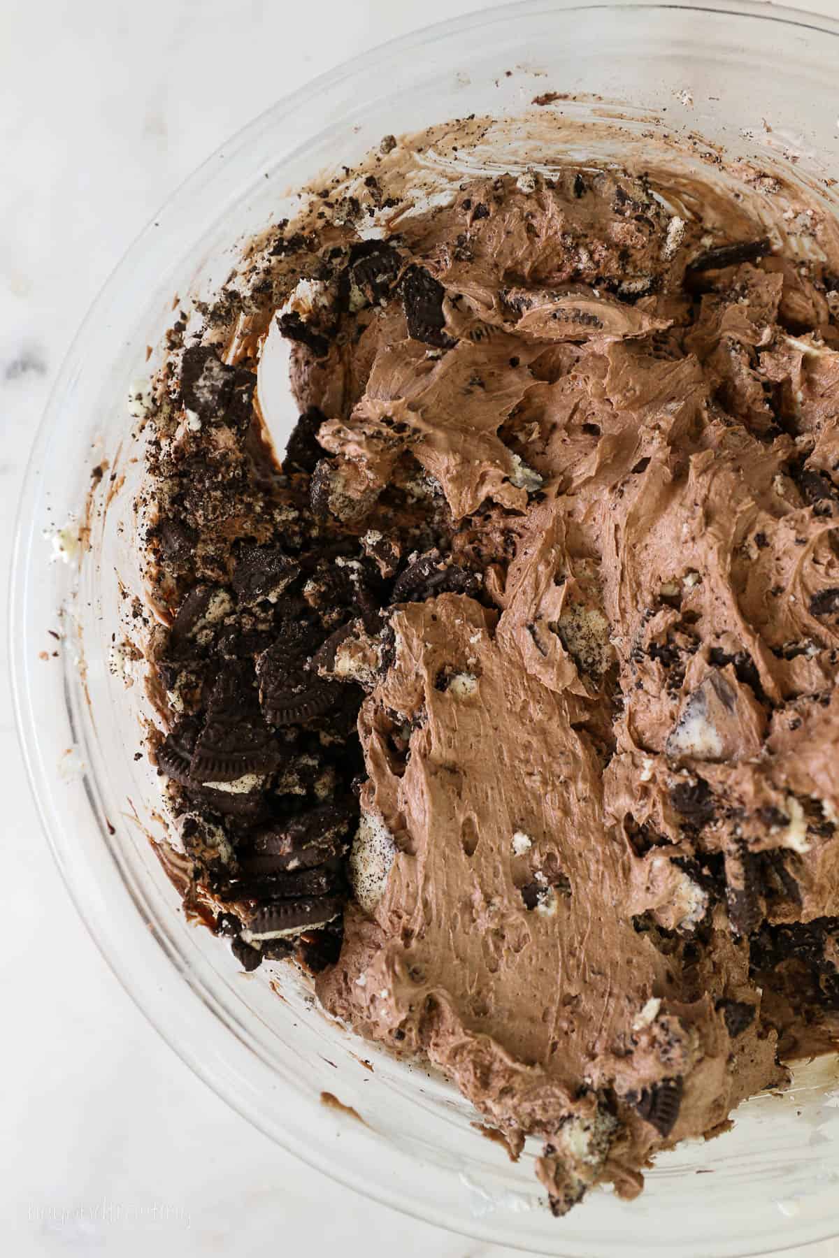 A glass mixing bowl with chocolate cheesecake batter and Oreos