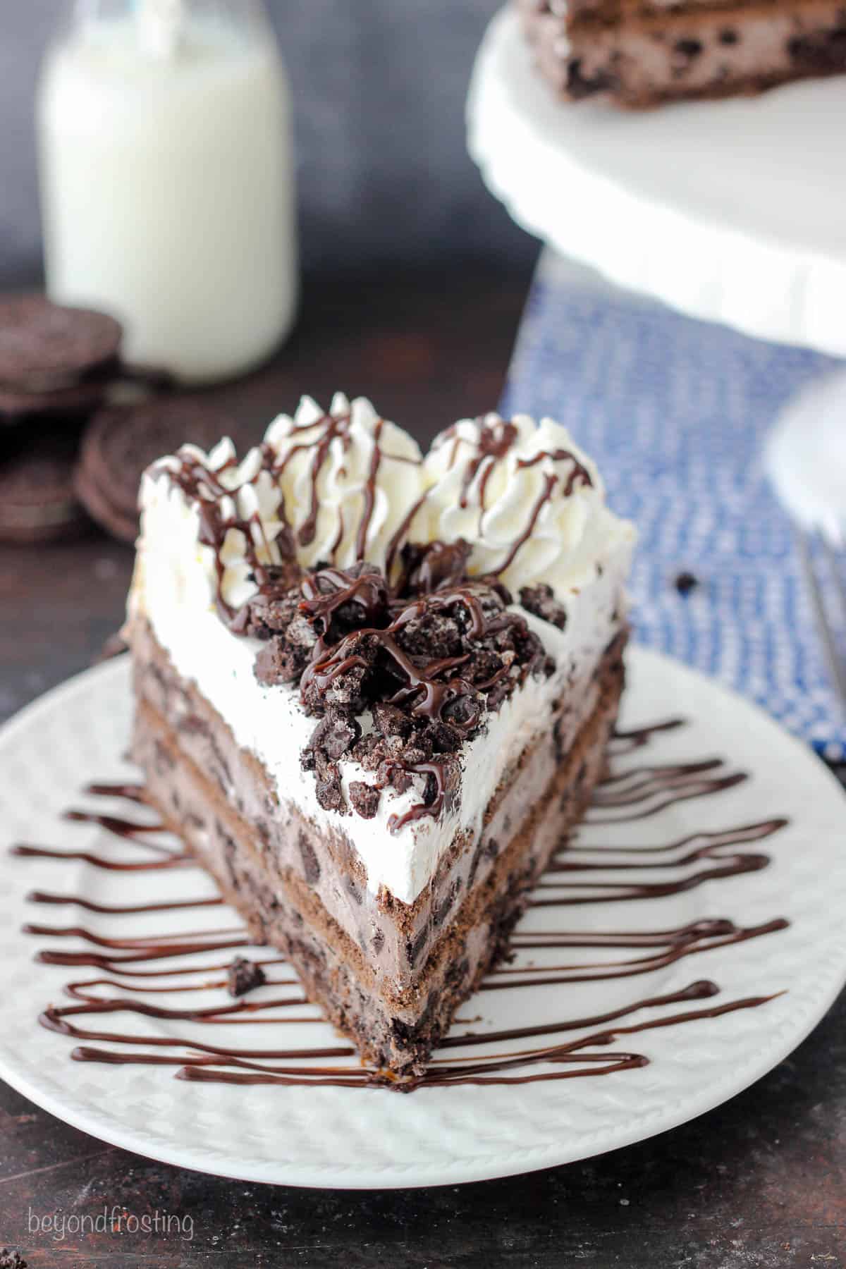 front view of a slice of Oreo cake on a white plate drizzled with fudge