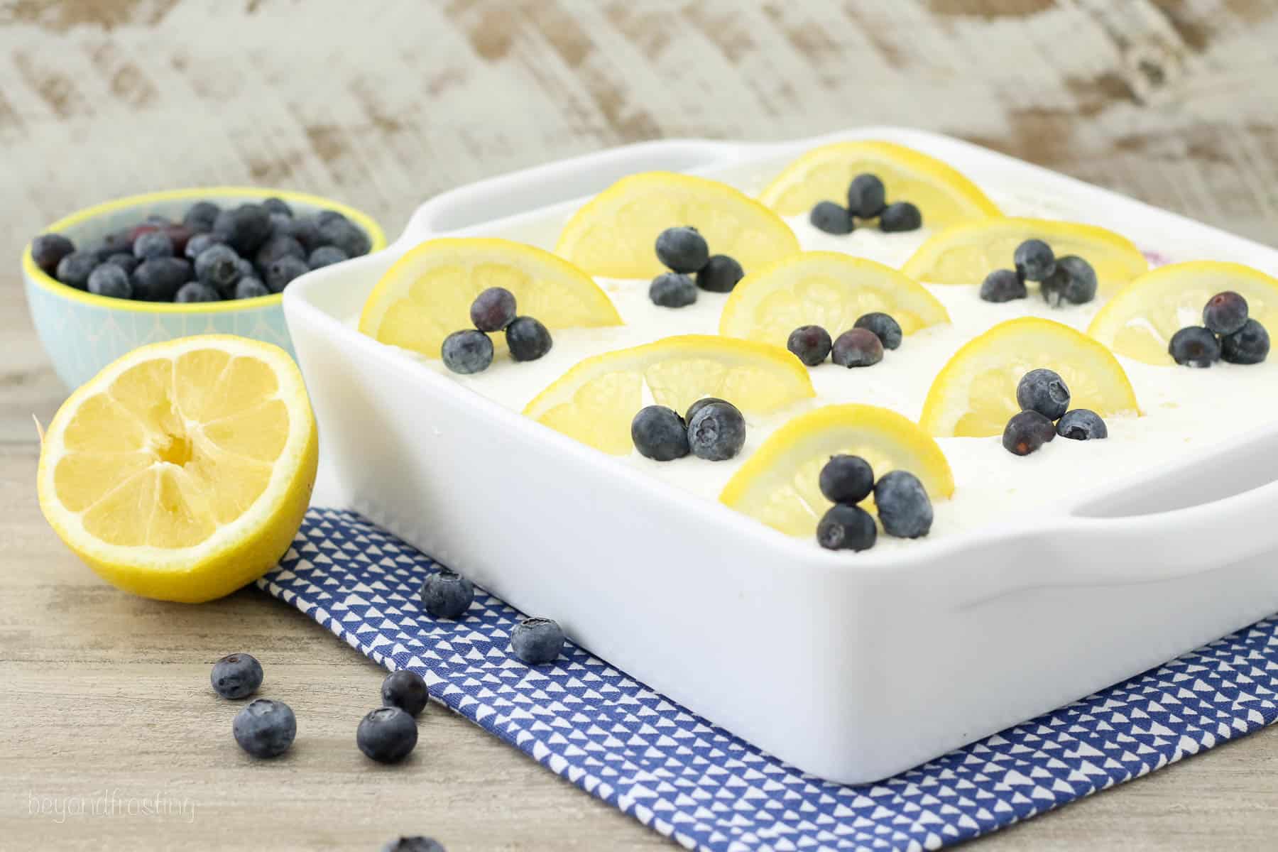 side view of a baking dish filled with a lemon icebox cake garnished with blueberries and lemon