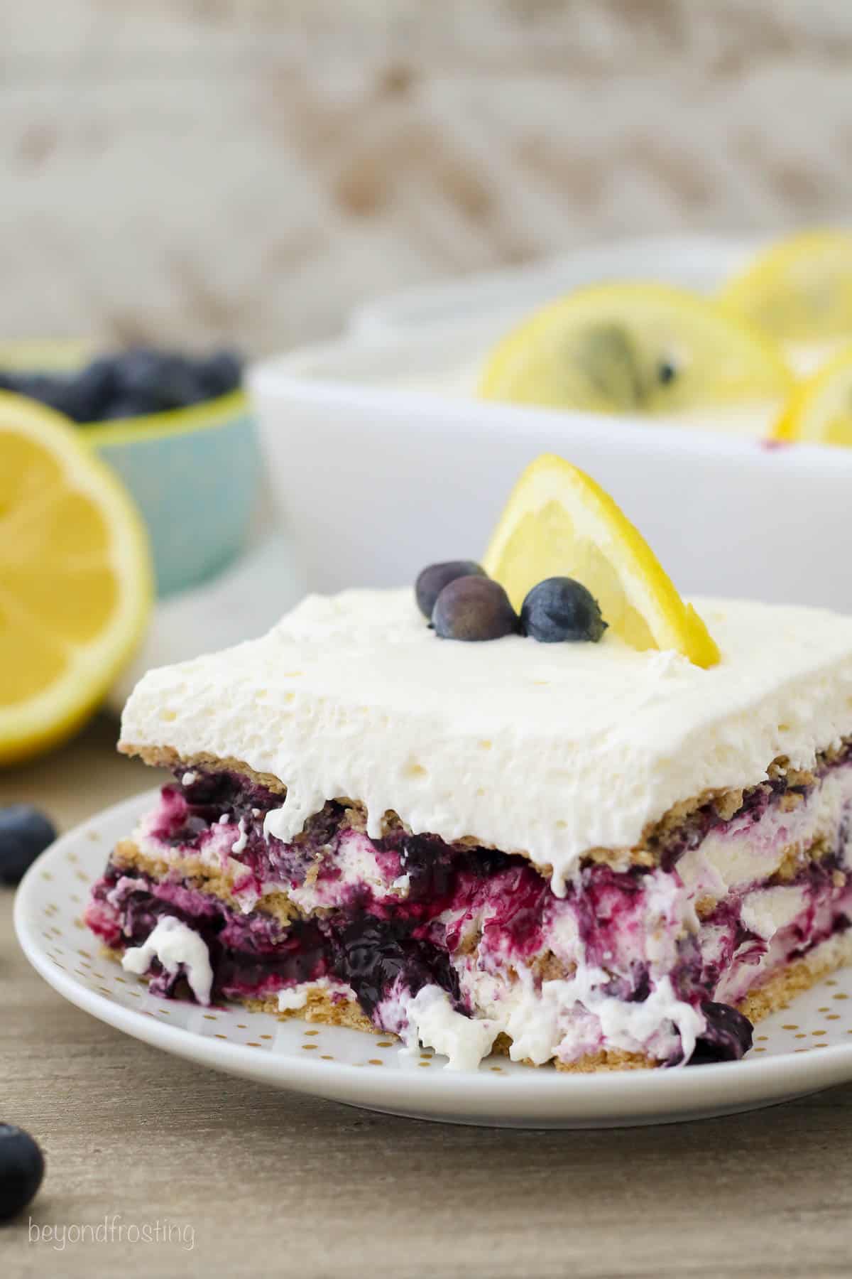 side view of a square of icebox cake on a plate topped with fresh blueberries and a lemon slice