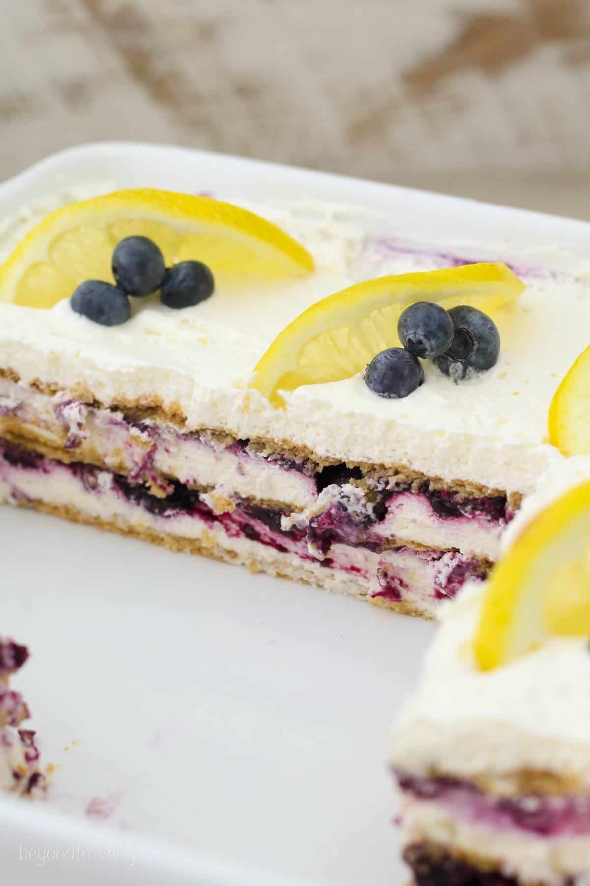 overhead of a half filled baking dish with lemon icebox cake garnished with blueberries and lemon slices