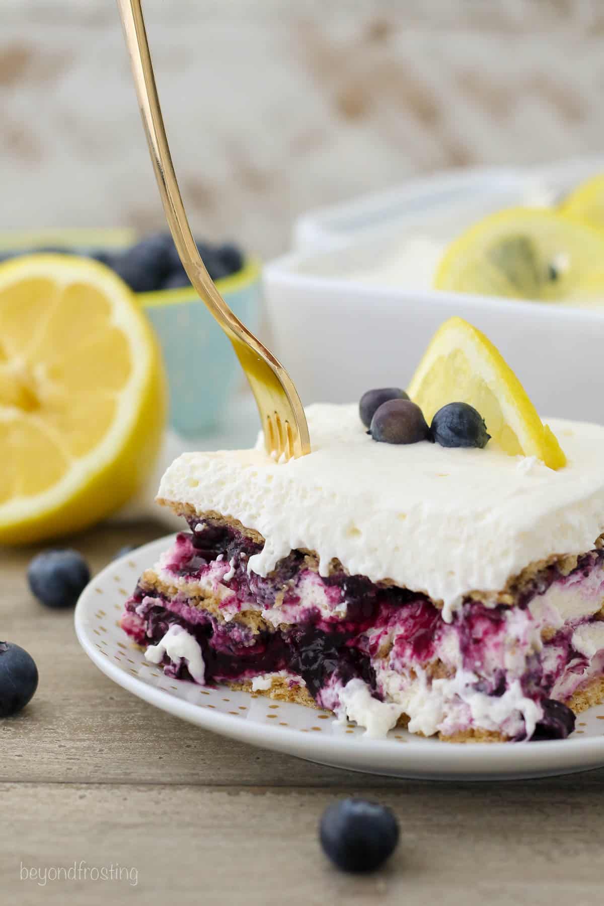 a fork being plunged into a square of blueberry lemon icebox cake on a plate
