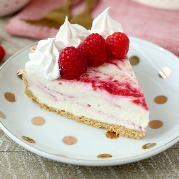 A slice of raspberry cheesecake on a gold polka dot plate