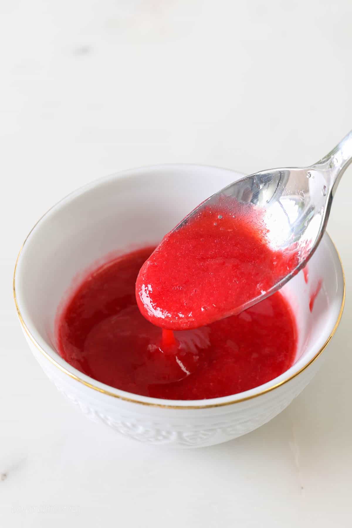Raspberry puree dripping off a spoon into a white bowl