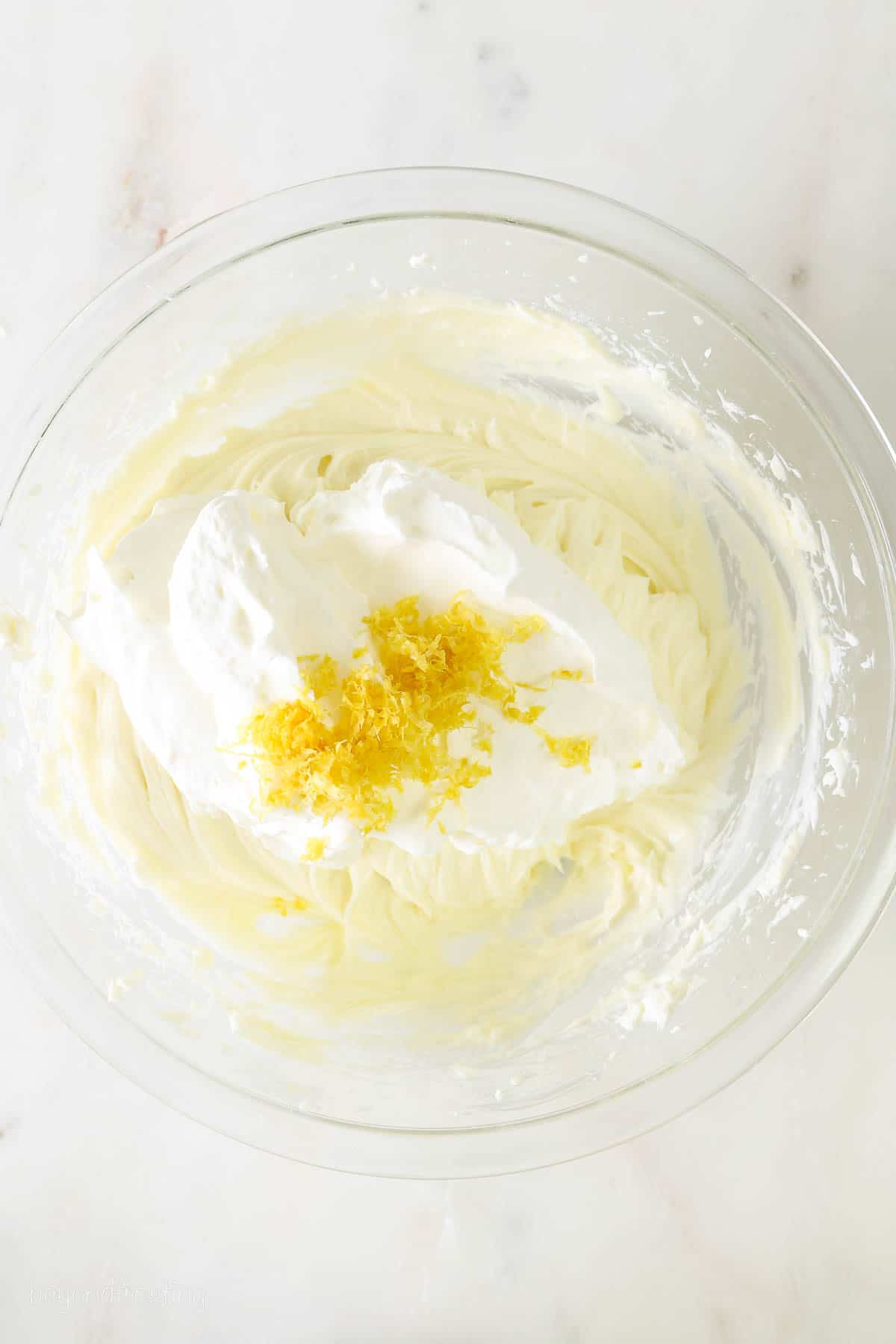 a glass mixing bowl with no-bake cheesecake filling, whipped cream and lemon zest