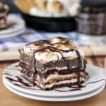 closeup of a slice of s'mores lasagna on a white plate drizzled with chocolate