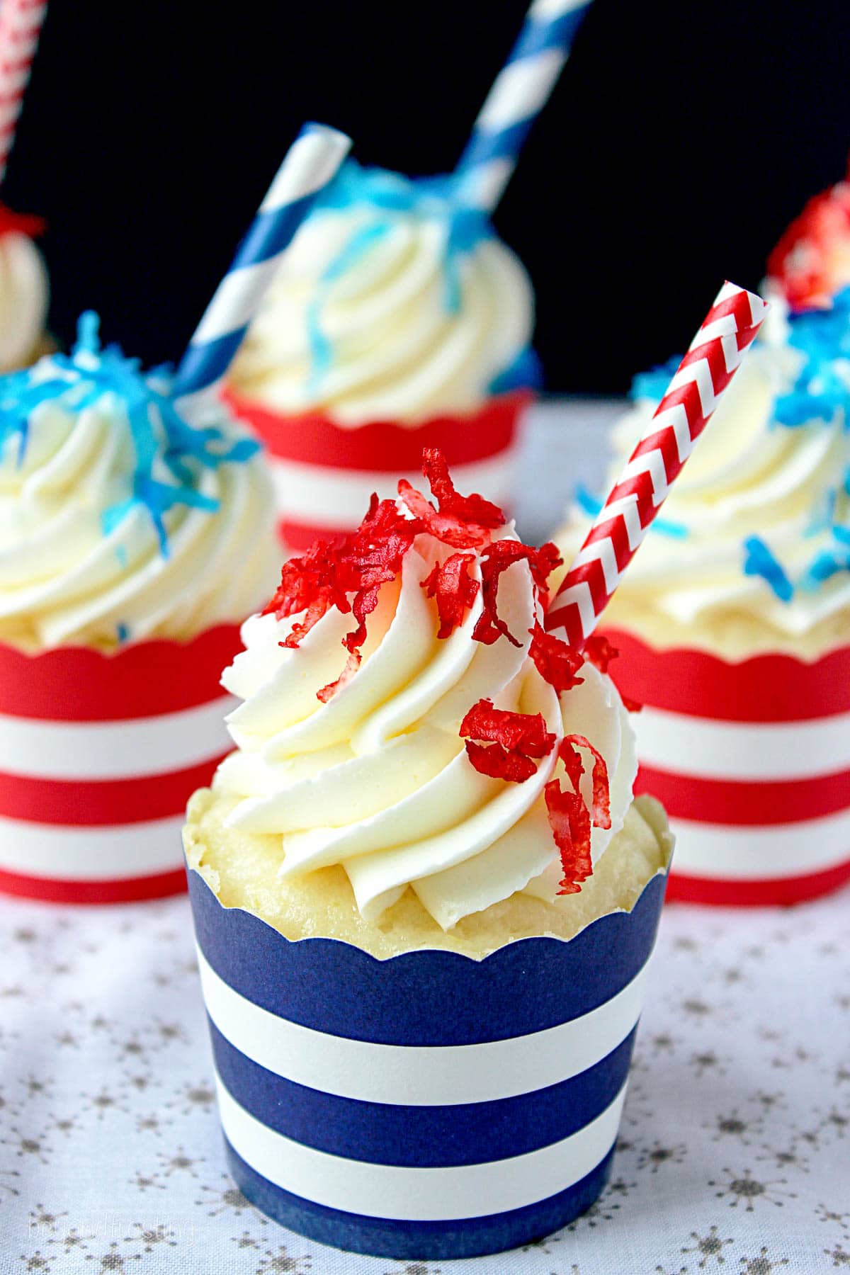 side view of a piña colada cupcake in a blue striped wrapper with more in the background