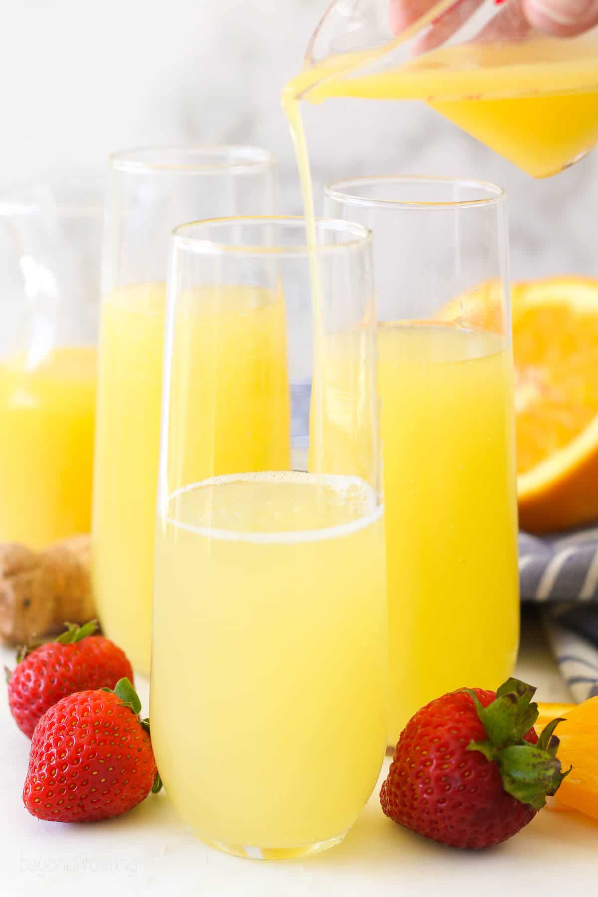 orange juice being poured into a stemless wine glass with prosecco