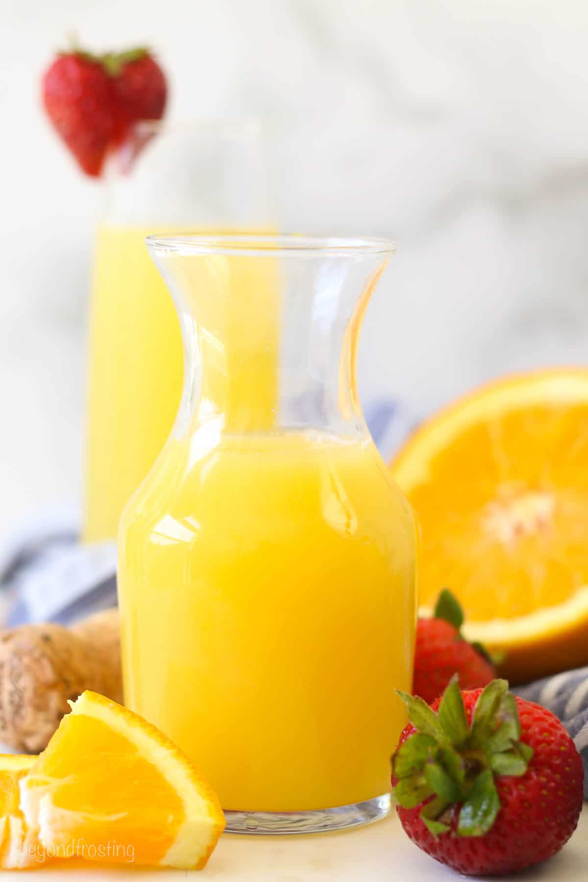 a small pitcher of orange juice surrounded by sliced oranges and strawberries