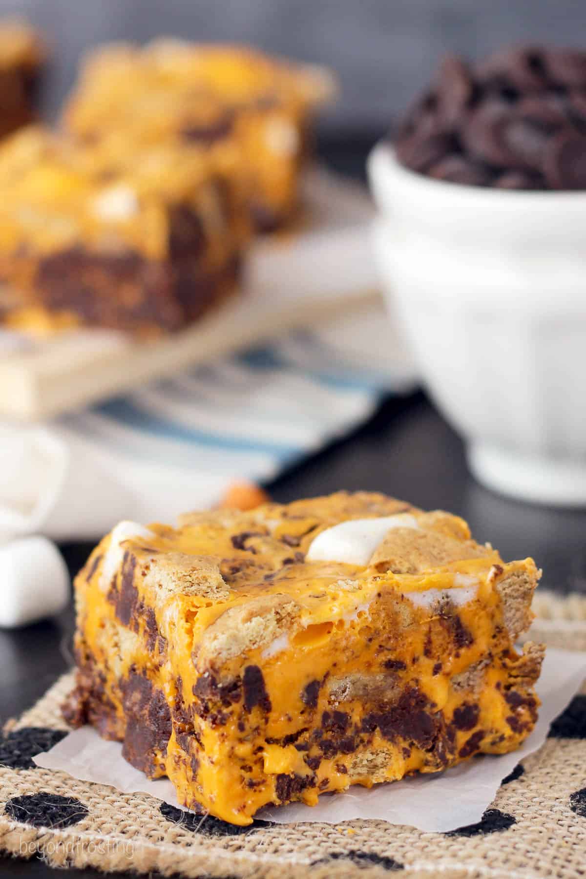 a square of pumpkin fudge with more fudge and a bowl of chocolate chips in the background