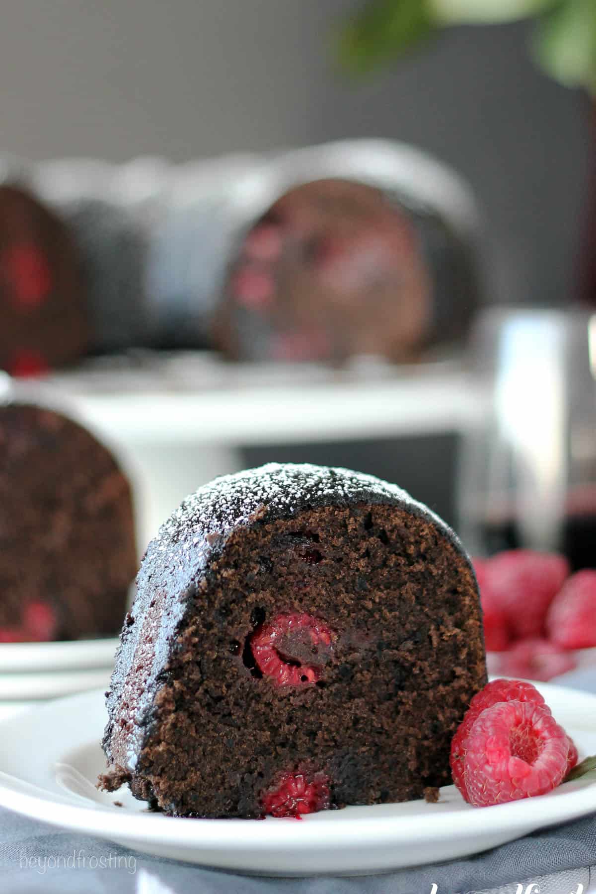 side view of a slice of raspberry cabernet cake on a plate with fresh raspberries