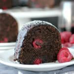 closeup of a slice of raspberry cabernet cake on a white plate garnished with fresh berries