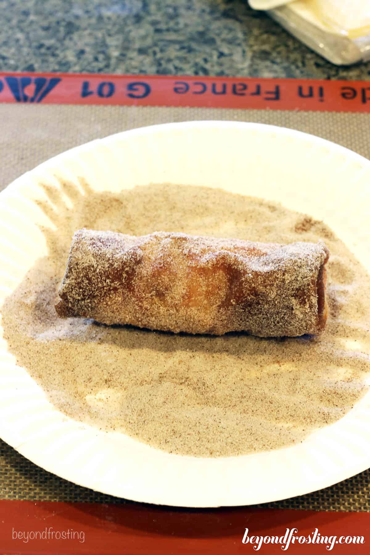a cheesecake egg roll being rolled in cinnamon and sugar