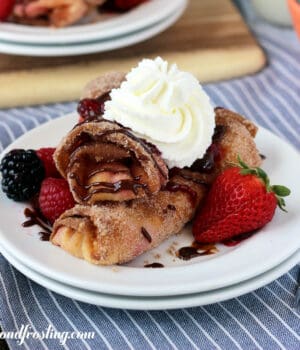 closeup of two raspberry cheesecake egg rolls on a plate garnished with whip and fresh berries