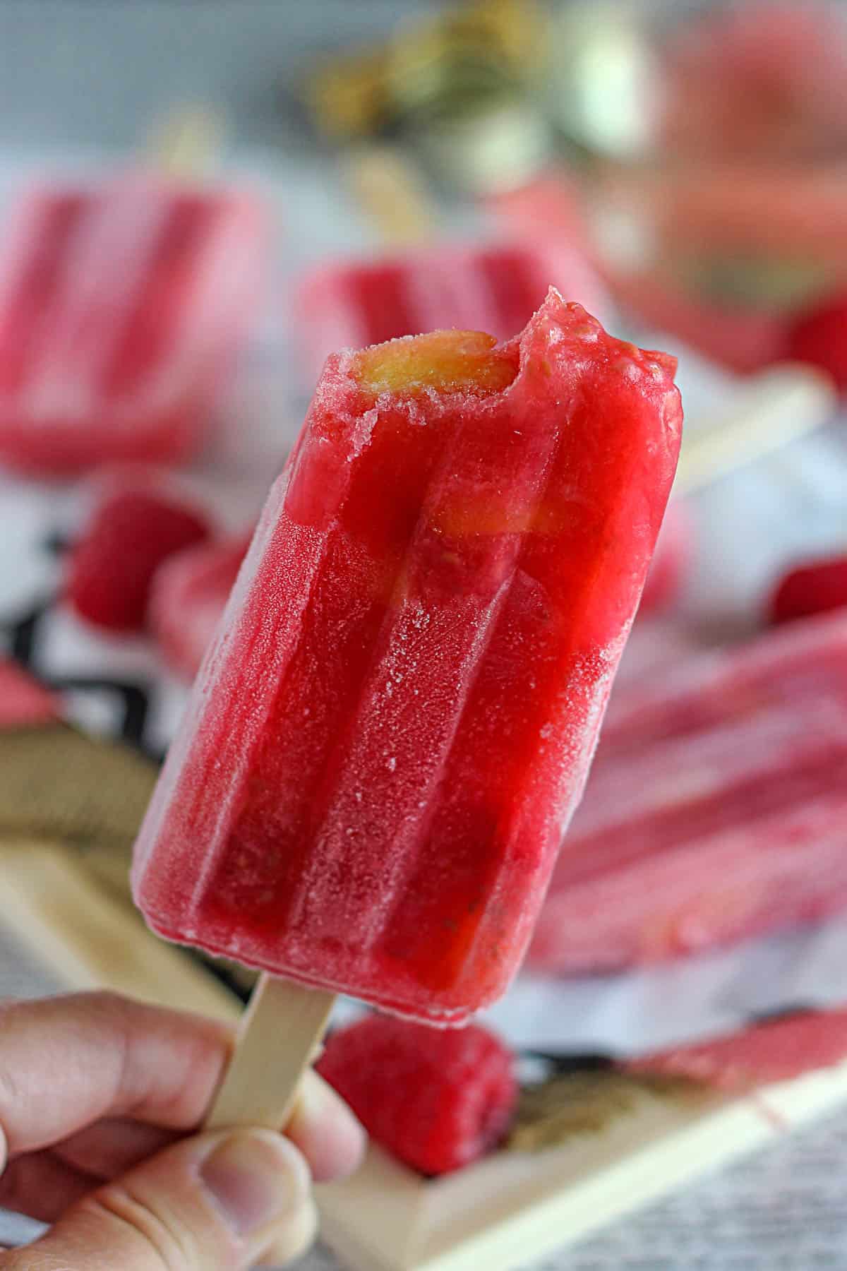 peach raspberry popsicle with a bite taken out held