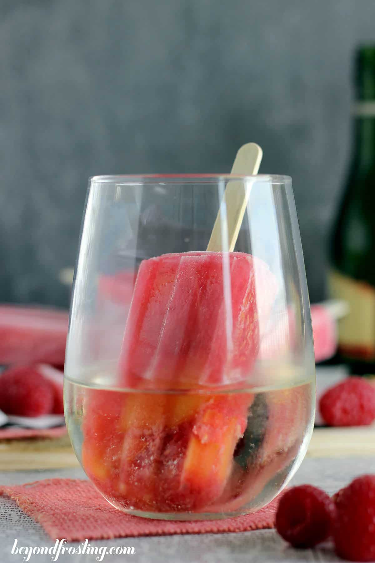 a peach raspberry popsicle in a glass of champagne