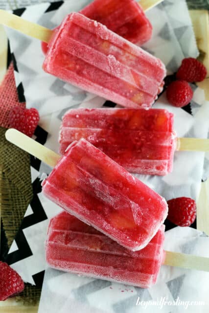overhead of five peach raspberry popsicles laying on a piece of parchment paper