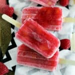 overhead of peach raspberry popsicles lying on a piece of parchment paper