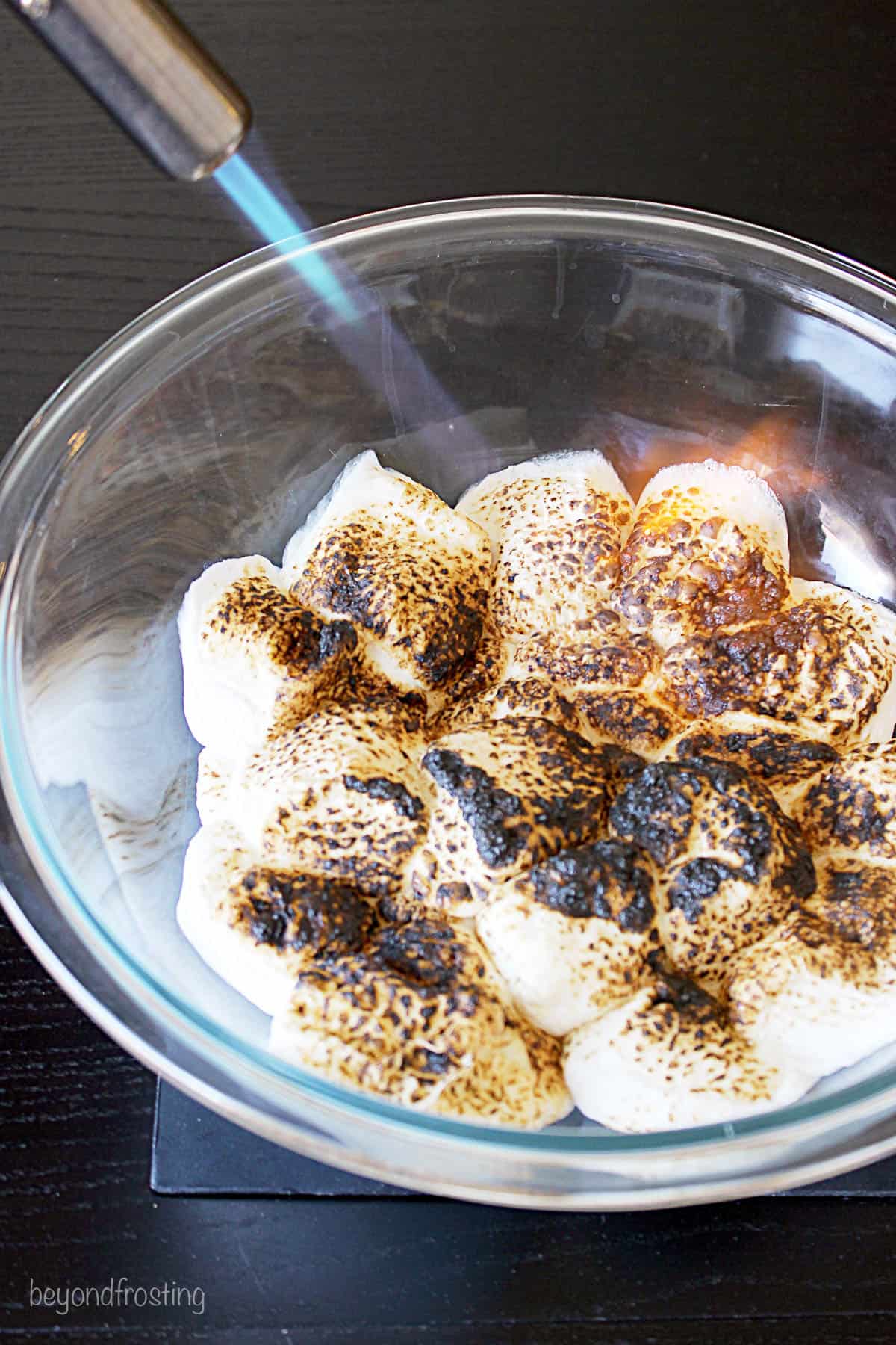 a bowl of marshmallows being toasted with a kitchen torch