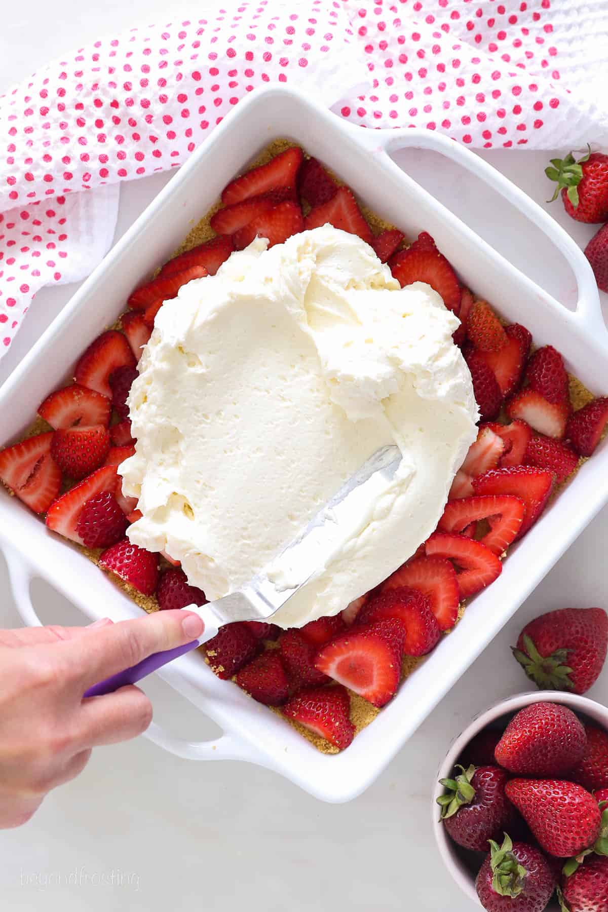 An angled spatula spreading cheesecake filling over top of strawberries