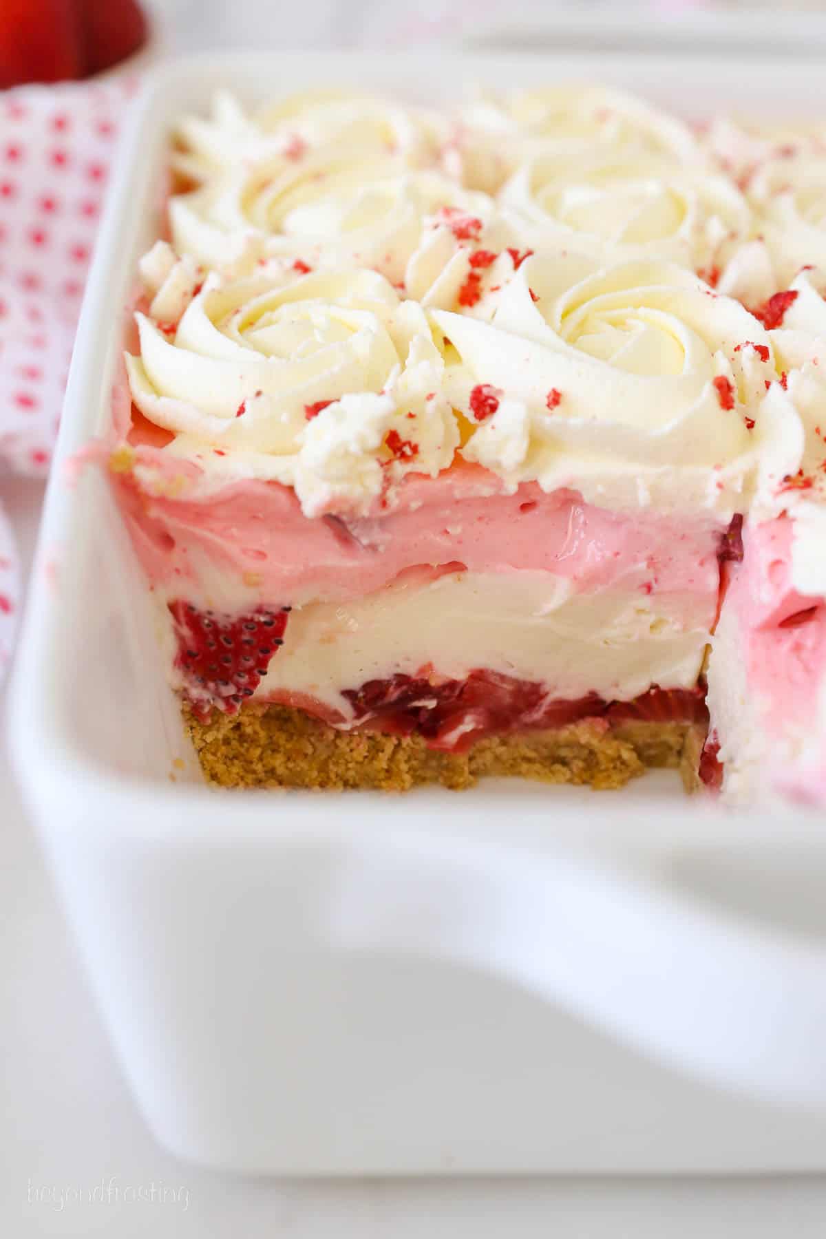 A white casserole dish with a layered strawberry dessert with a piece missing