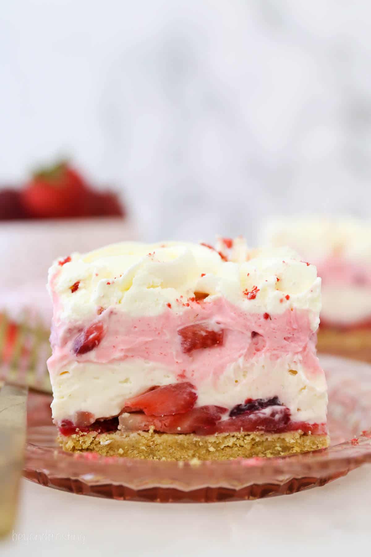a slice of layered strawberry delight on a pink plate with a gold fork
