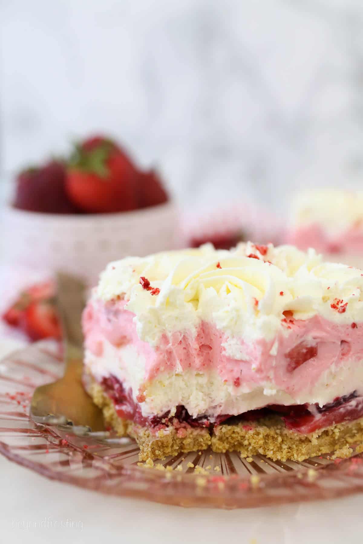 a pink glass plate with a slice of strawberry delight with bites missing