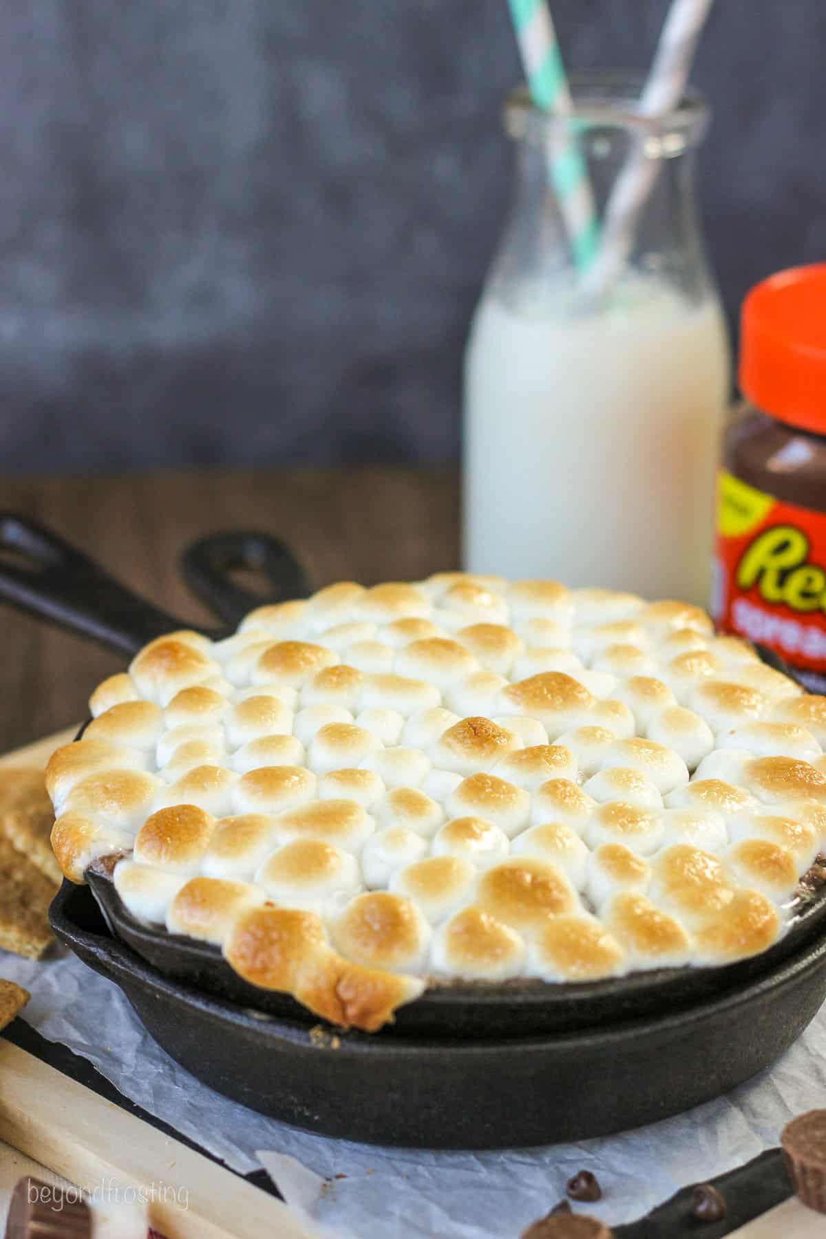 side view of a skillet filled with peanut butter s'mores dip with a jar of milk in the background