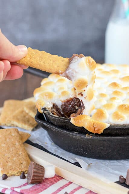 a graham cracker being dipped into a pan full of peanut butter s'mores dip