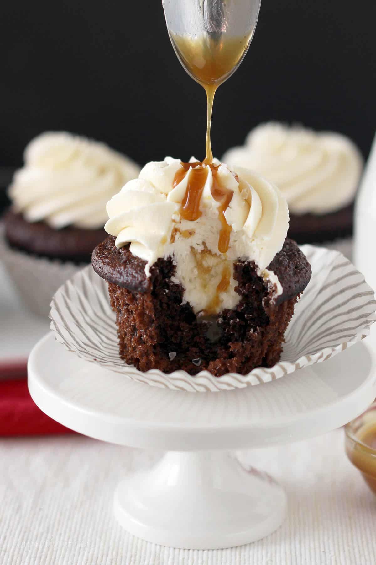 a chocolate cupcake with a bite taken out being drizzled with caramel sauce
