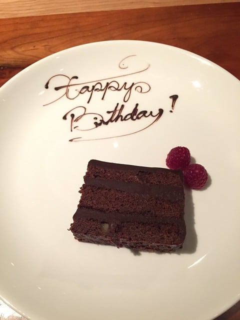 A slice of chocolate cake on a plate with happy birthday written in chocolate