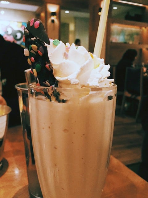 Side view of a milkshake with a piece of chocolate covered bacon sticking out the top