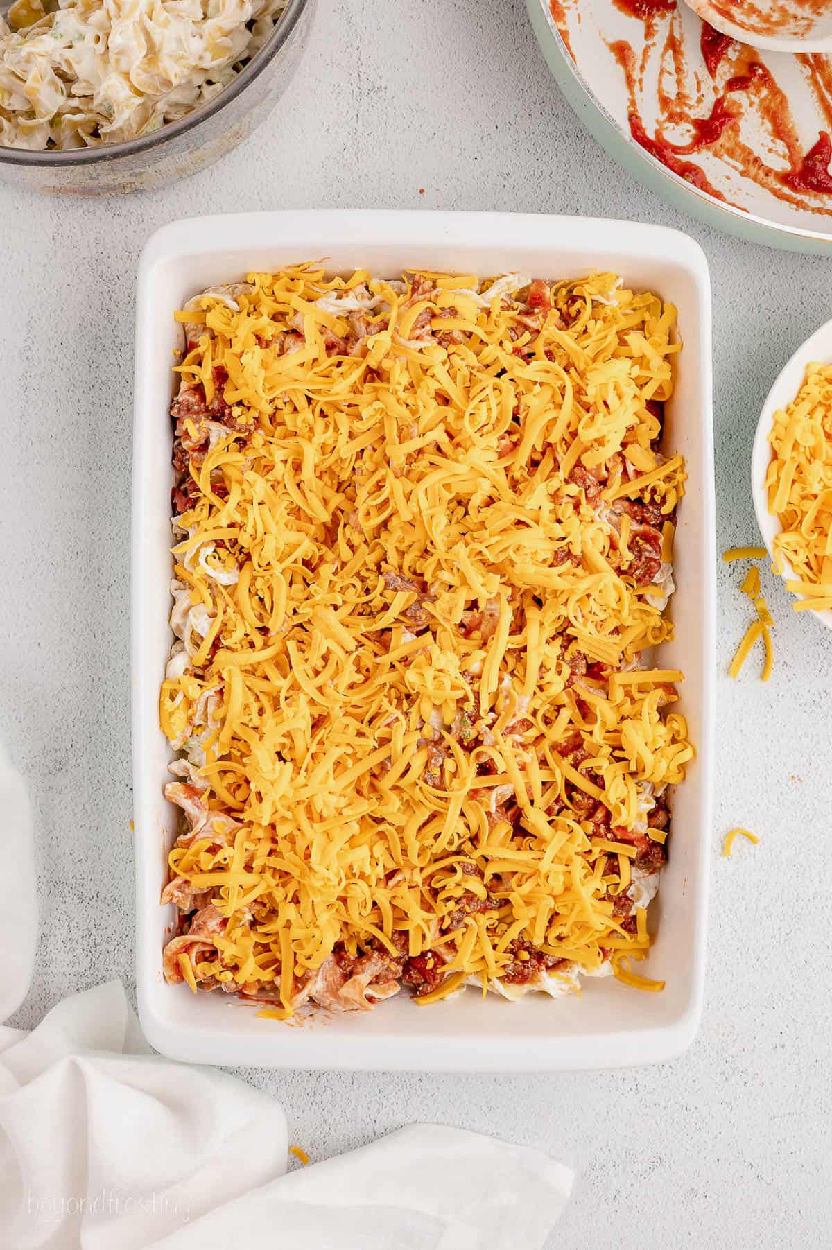 Cheddar cheese on top of noodles in a casserole dish