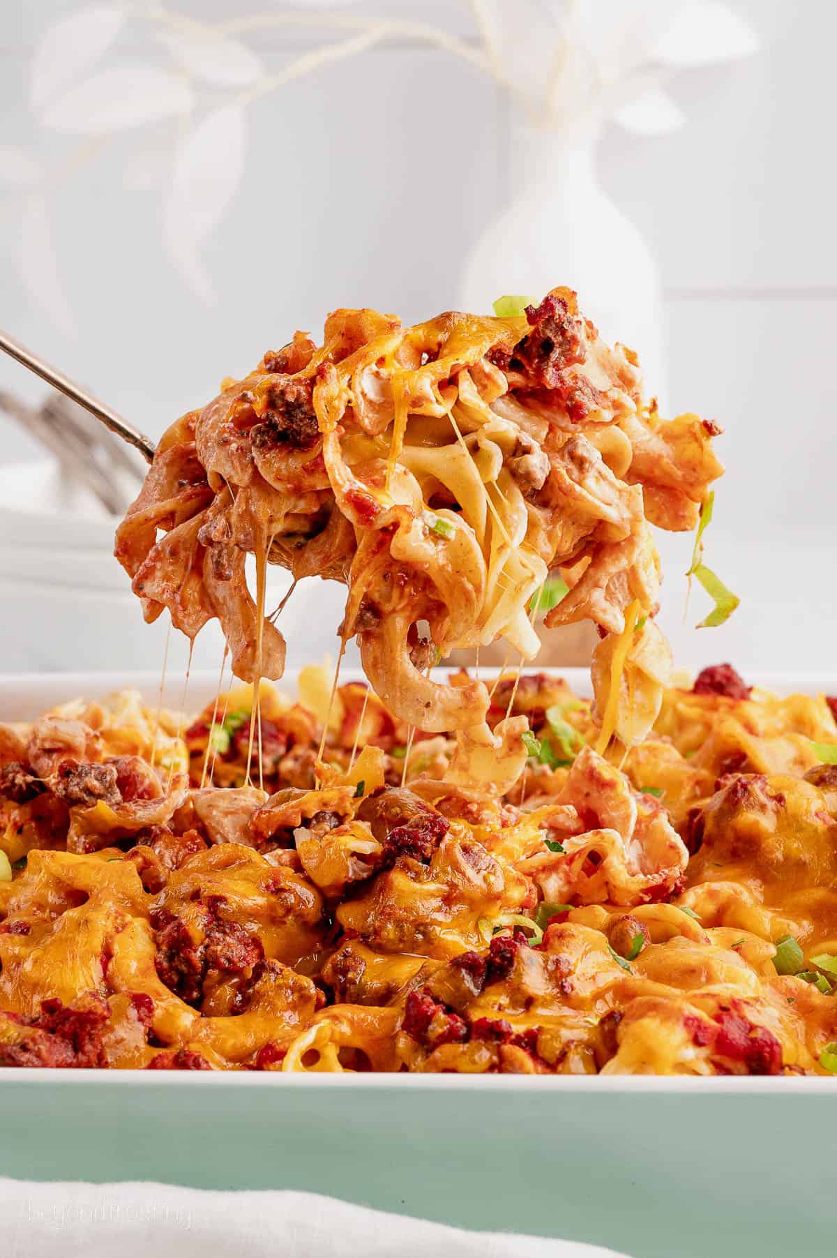 A spoon serving cheesy ground beef noodle casserole
