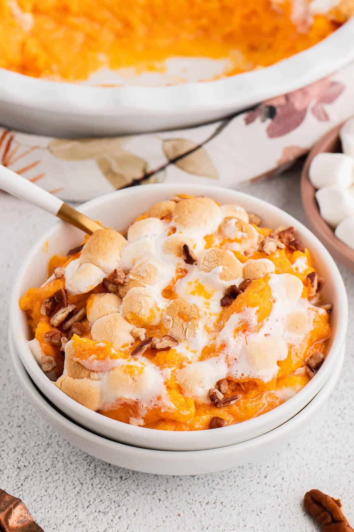Serving of marshmallow-topped sweet potato casserole sits next to casserole dish.