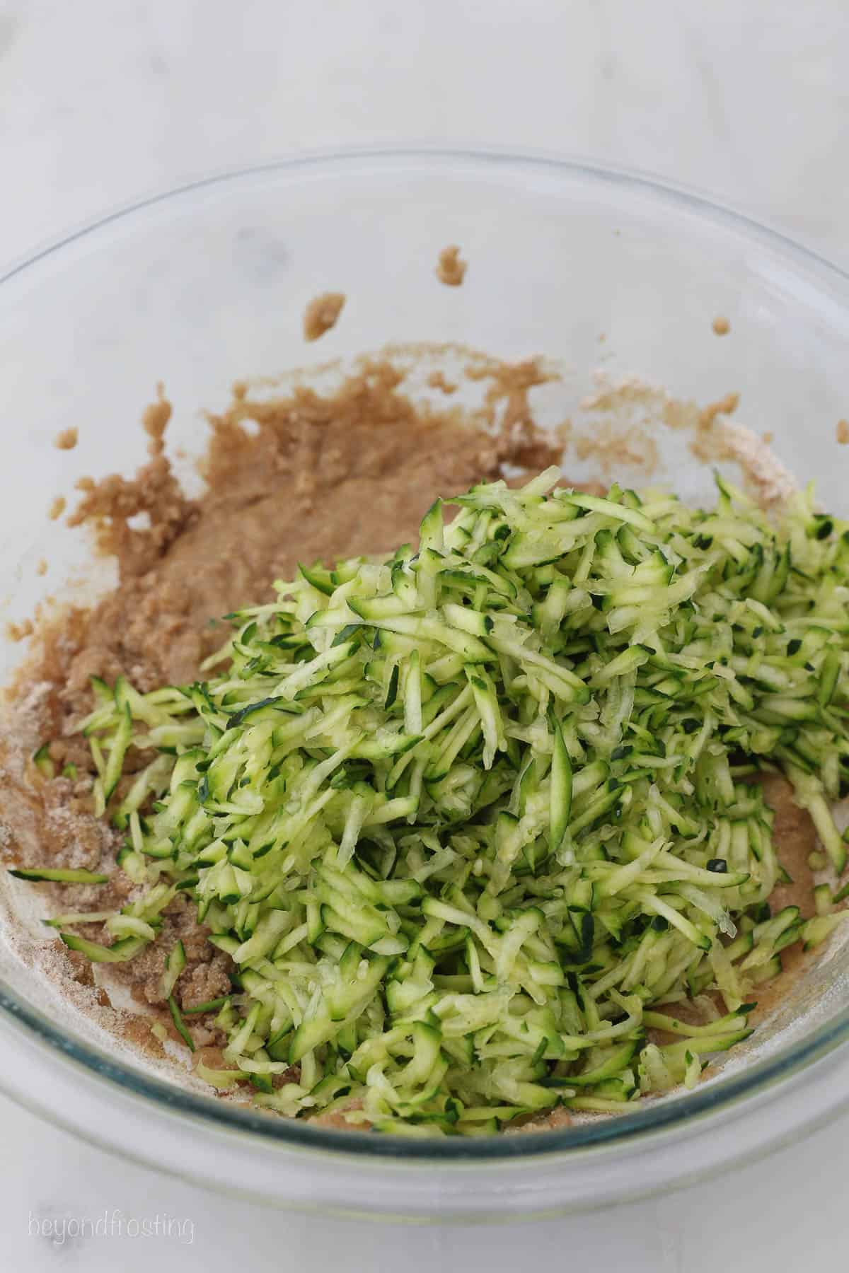 grated zucchini and batter for zucchini bread in a glass mixing bowl