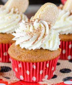 closeup of a pumpkin cupcake in a red and white liner with whipped cream and a cookie