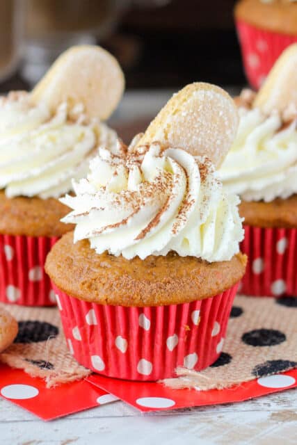 side view of a pumpkin cupcake topped with whip and a cookie