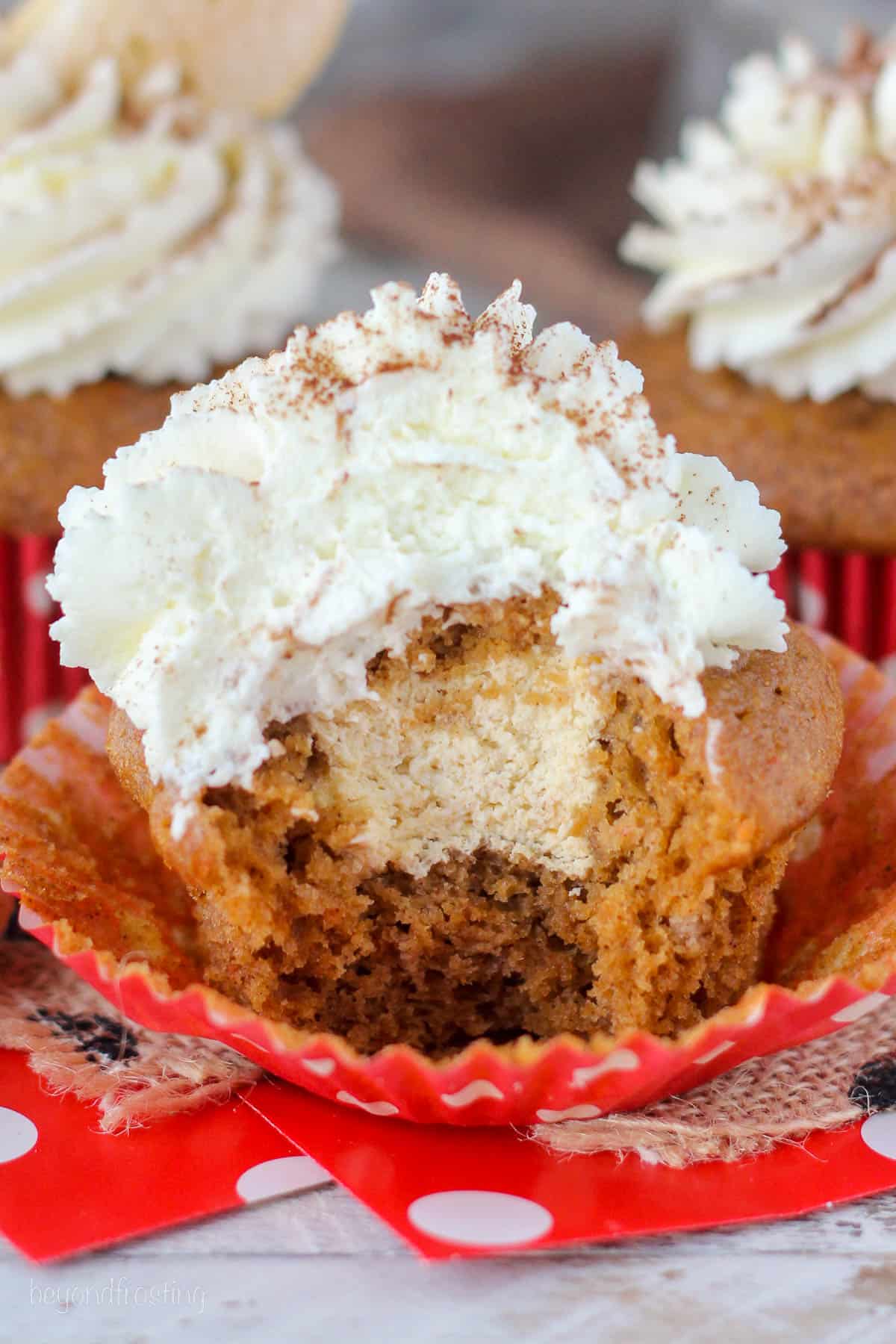 closeup of a pumpkin cupcake topped with whip with a bite taken out of it