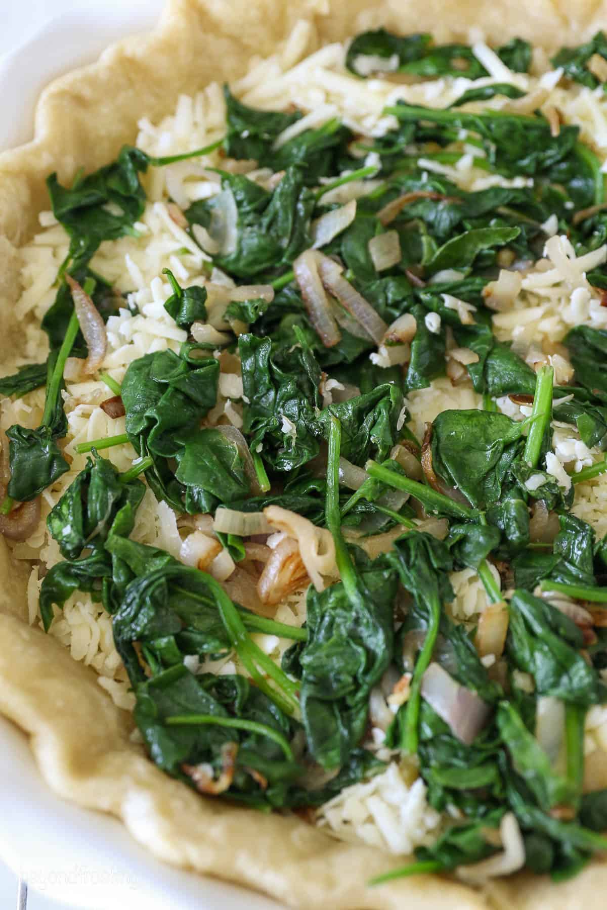 Shredded cheese topped with spinach in a pie crust