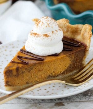 a slice of spiced pumpkin pie on a plate topped with chocolate ganache and whipped cream