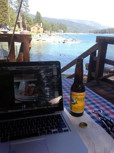 A laptop and a beer on a deck table overlooking the lake