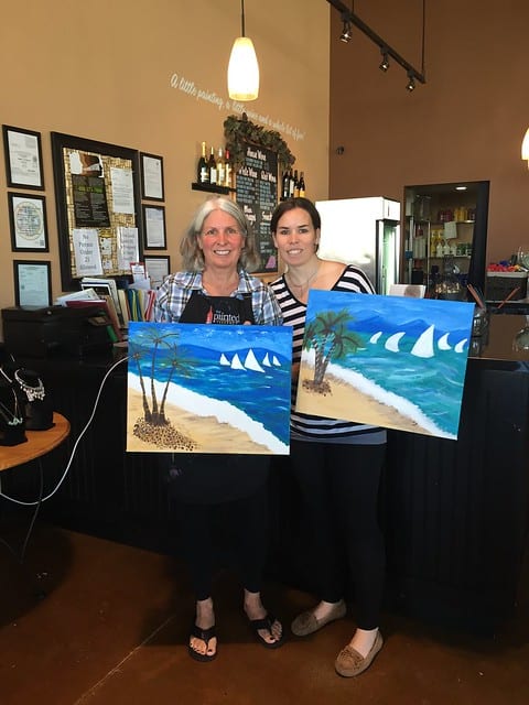 Blog author and her mom holding their completed paintings at a Paint and Sip event