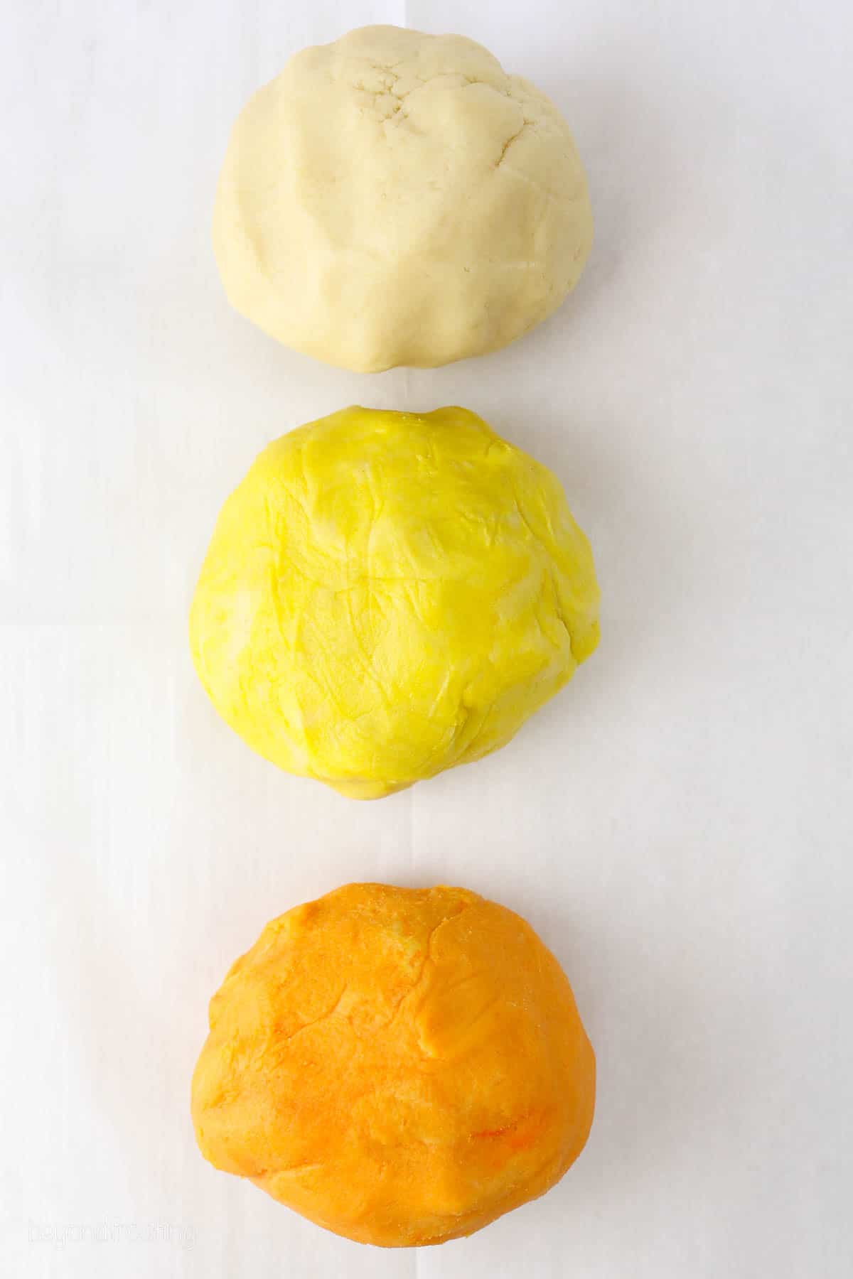 Three large portions of sugar cookie dough colored white, yellow, and orange.
