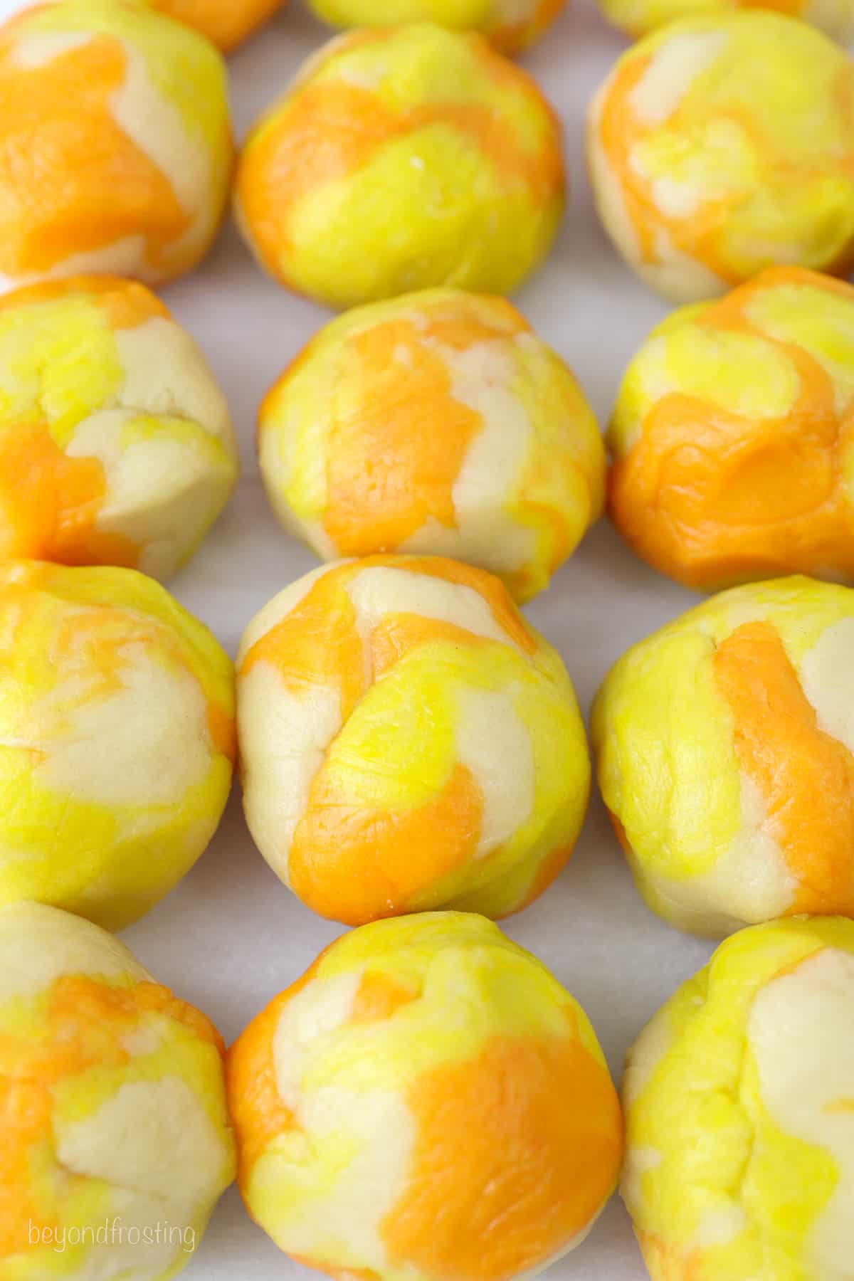 cookie dough balls lined up on parchment paper. They are colored yellow, orange and white.