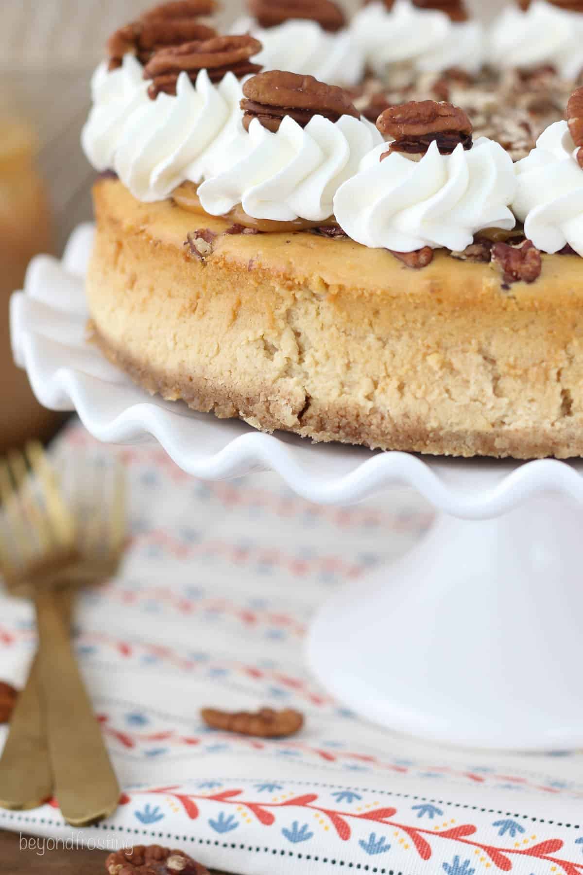side view of a whole caramel pecan cheesecake on a cake stand