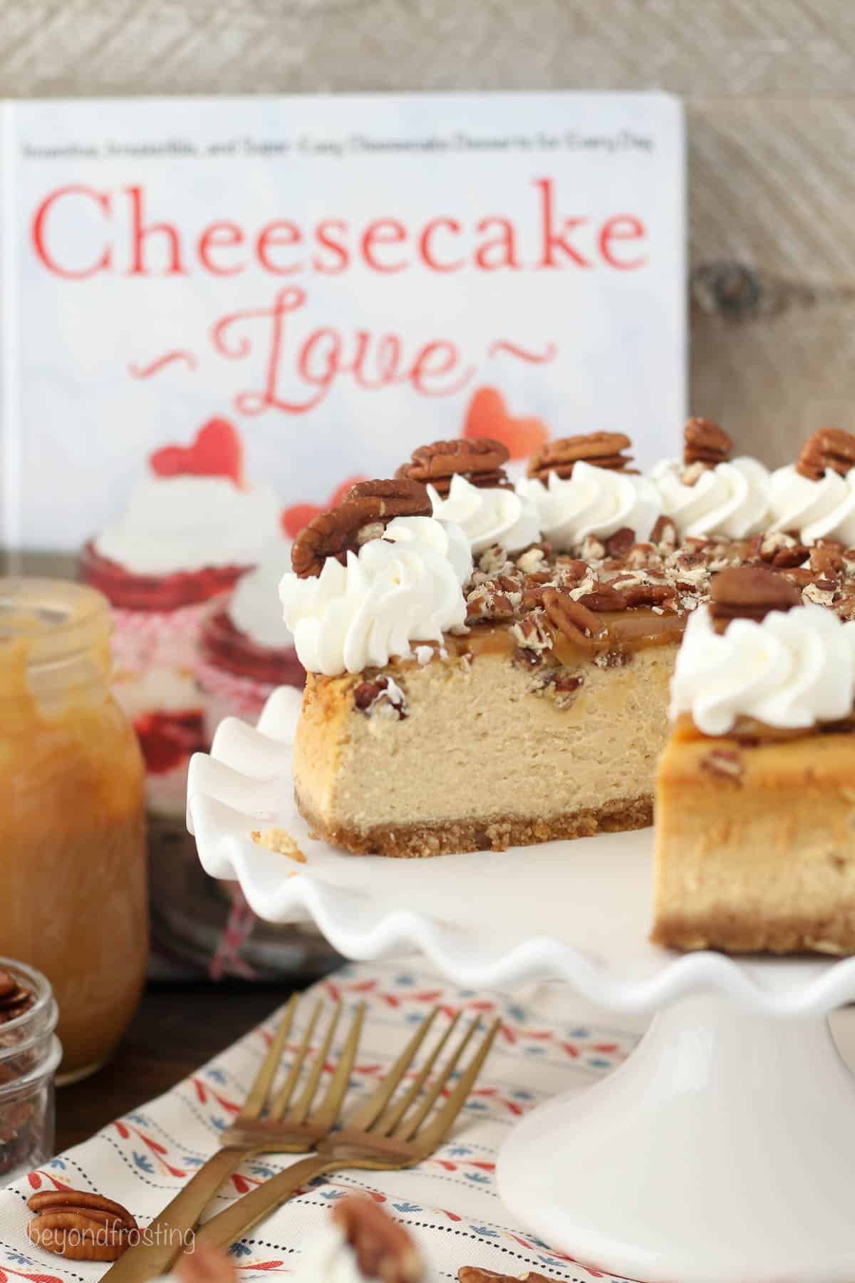 a caramel cheesecake on a cake stand in front of a book titled "Cheesecake Love"