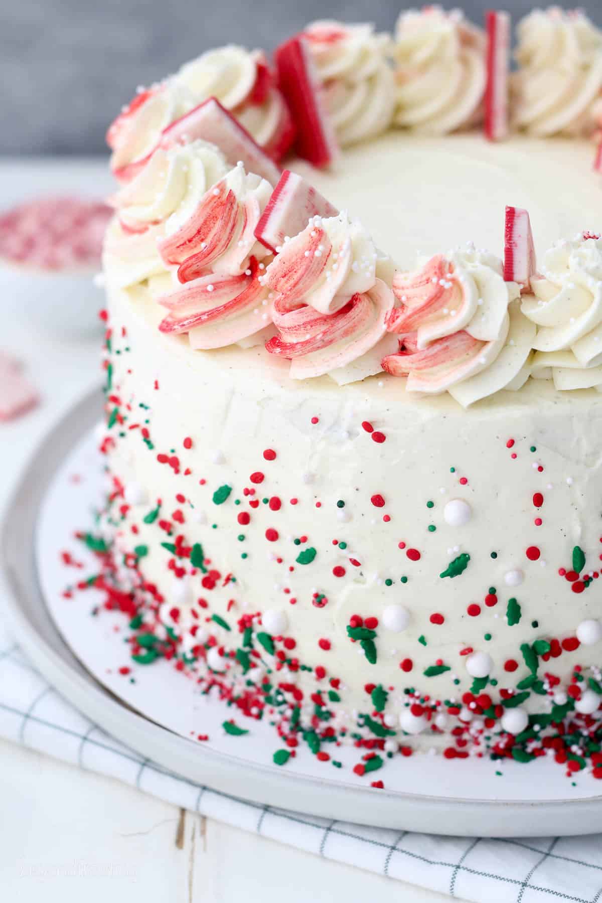 overhead of a whole chocolate peppermint cake on a plate garnished with peppermint bark and red and green sprinkles