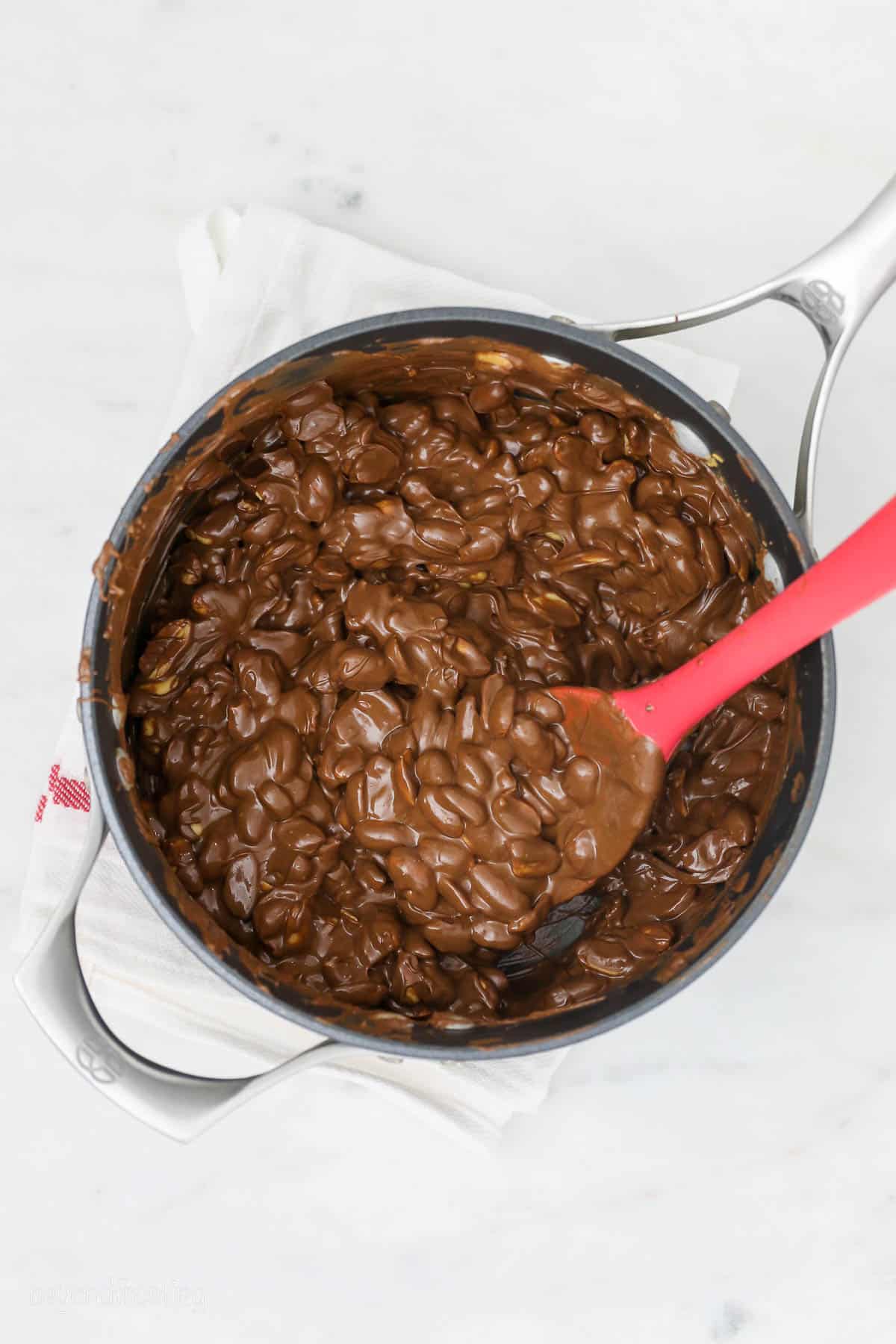 overhead of melted chocolate and peanut butter mixed with peanuts in a saucepan with a red spoon
