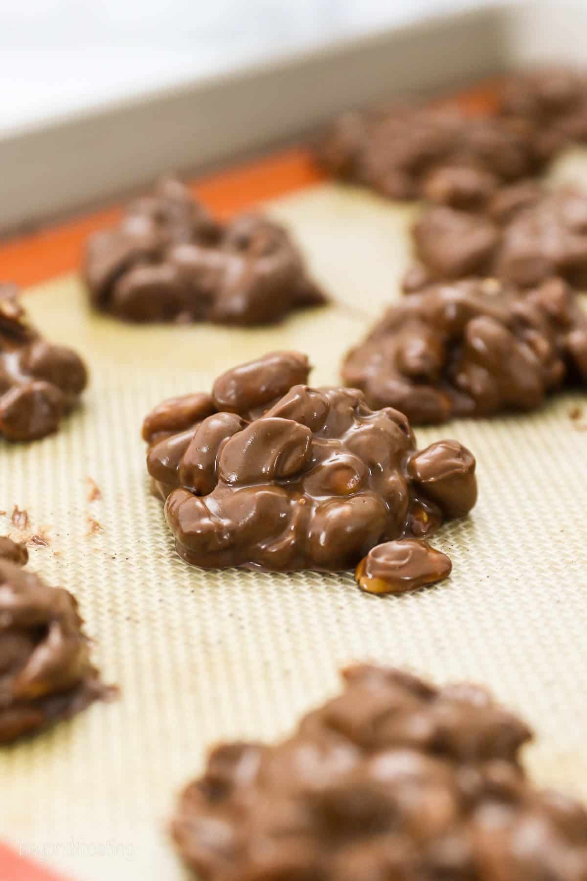 scoops of melted chocolate and peanuts dropped onto a lined baking sheet